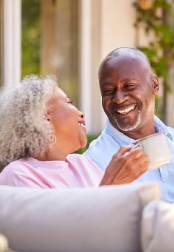 Retired Couple Sitting Outdoors At Home Having Morning Coffee Together